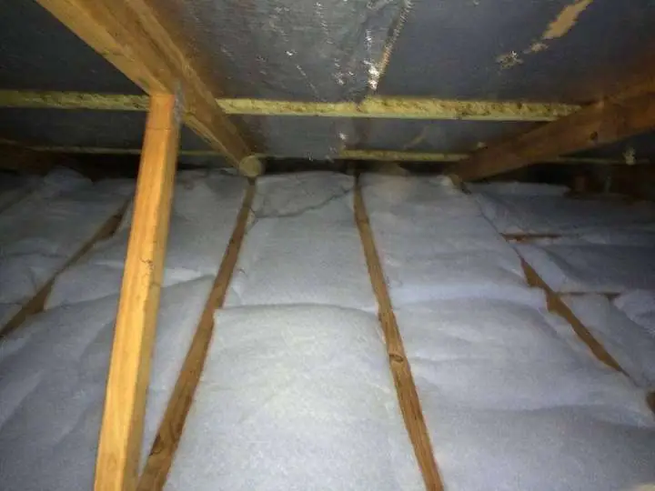 Bright white polyester batts laid neatly wall-to-wall between ceiling joists under a metal roof — Ashgrove