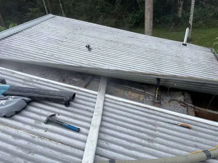 An installer's tools on a corrugated iron roof with the ridge opened to pump cellulose into a raked ceiling section — Mount Burrell