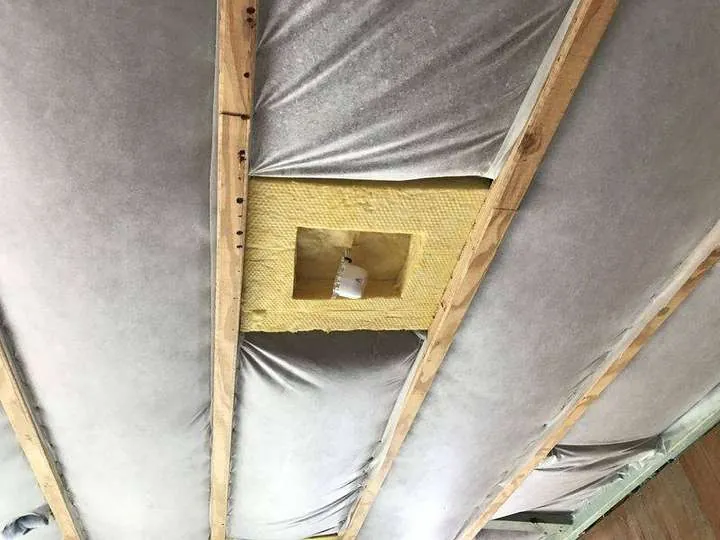 Grey sound-insulation matting stapled between the floor joists of a two-storey home, with a batt patch fitted around a downlight box — Carina, 2016
