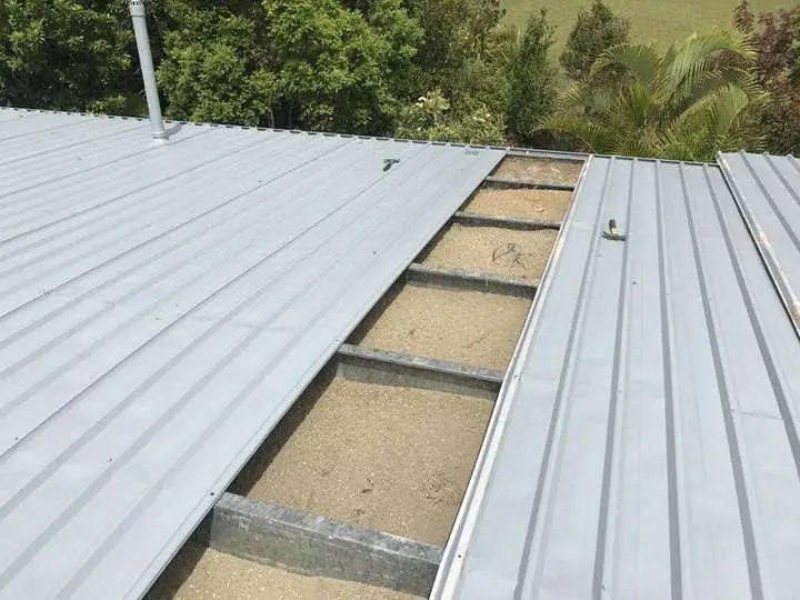 A trim-deck metal roof opened mid-job showing cellulose insulation packed between the steel battens — Mapleton, 2017